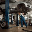 VW Tiguan auf einer Hebebühne wo gerade eine Felge abmontiert ist und ein KFZler sich die Vorderradaufhängung kontrolliert.
