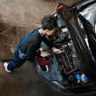 Junge Frau in Arbeitsbekleidung die gerade am Motorraum arbeitet von einem Seat 